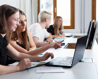 Vier Studierende mit Laptops in Seminarraum von der Seite