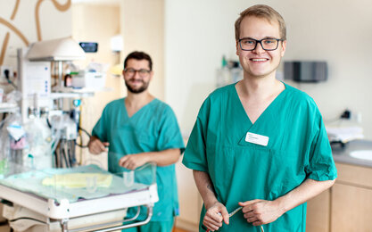 Zwei Männer in türkisenem Kasack an Baby Intensivbett