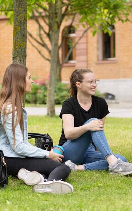 Drei Studierende sitzen auf der Campus Wiese und unterhalten sich