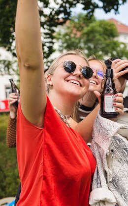 Drei Studierende feiern mit Bierflaschen auf dem Campus
