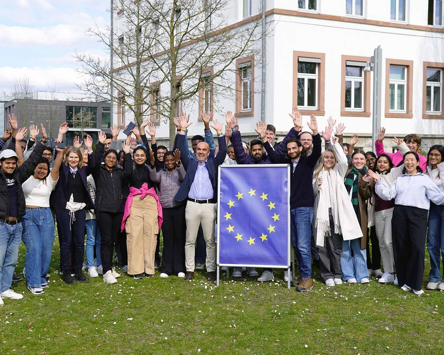 Gruppe der Studierenden mit Gastreferent, EU-Schild und alle heben die Hände