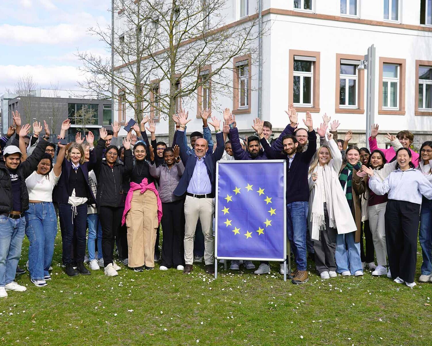 Gruppe der Studierenden mit Gastreferent, EU-Schild und alle heben die Hände