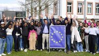 Gruppe der Studierenden mit Gastreferent, EU-Schild und alle heben die Hände