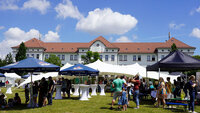 Gebäude der Hochschule im Hintergrund und Menschen unter Sonnenschirmen an Ständen im Vordergrund