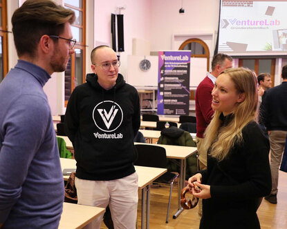 Janine Weirich, Co-Founderin der xeem GmbH, steht in der Aula mit zwei männlichen Teilnehmenden zusammen und unterhält sich mit ihnen