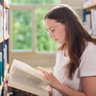 Studentin liest in Buch in der Bibliothek