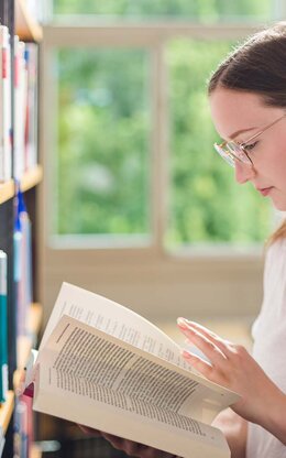 Studentin liest in Buch in der Bibliothek