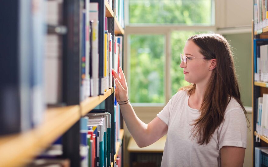 Studentin sucht Buch in Buchregal in Bibliothek