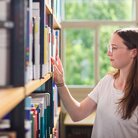 Studentin sucht Buch in Buchregal in Bibliothek