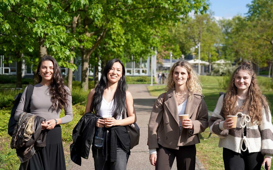 Vier Studentinnen lachen in die Kamera im Freien auf dem grünen Campus