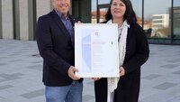 Ein Mann und eine Frau stehen vor einem TH-Gebäude mit der Urkunde in der Hand
