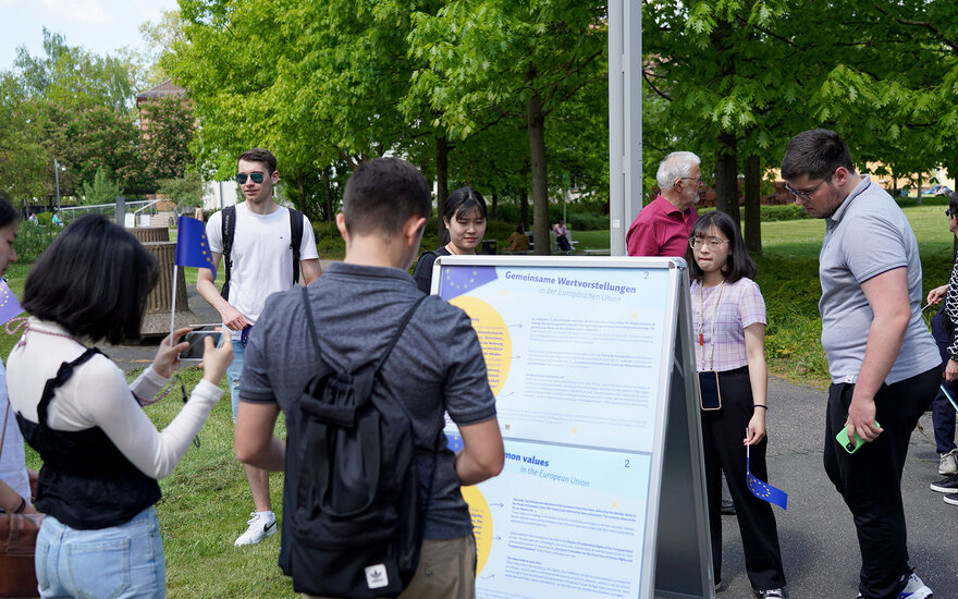 Junge Menschen betrachten im Freien auf dem Campus eine Tafel über gemeinsame Wertvorstellungen