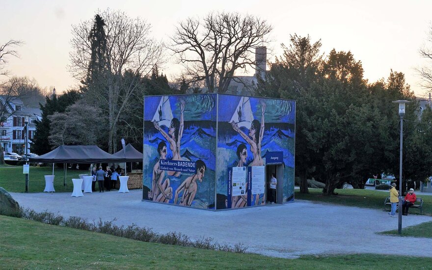 Ausstellungskubus mit Gemälden von Kirchner an der Außenwand und Besuchern der Eröffnung in Königstein