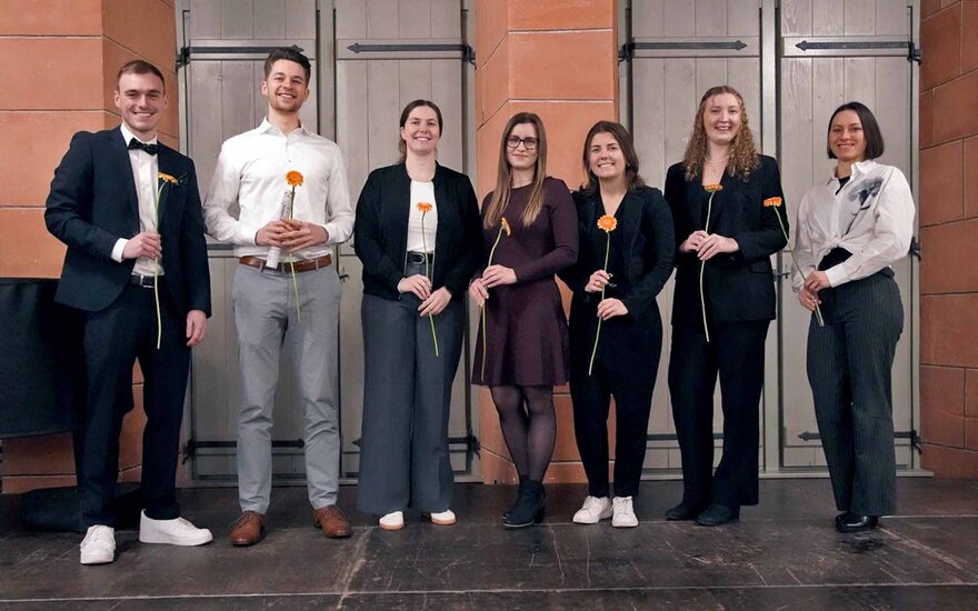 Gruppenfoto mit sieben Absolventinnen und Absolventen mit Rosen in der Hand
