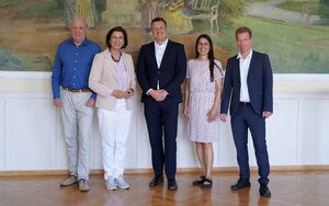 Ministerialdirigent Dr. Haaf steht im schwarzen Anzug eingerahmt von den vier Mitgliedern der Hochschulleitung vor einem Wandgemälde im Hocksaal der Hochschule und blickt lächelnd in die Kamera