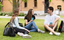 Drei Studierende sitzen auf der Campus Wiese und unterhalten sich, nachhaltiger Kaffee To Go Becher