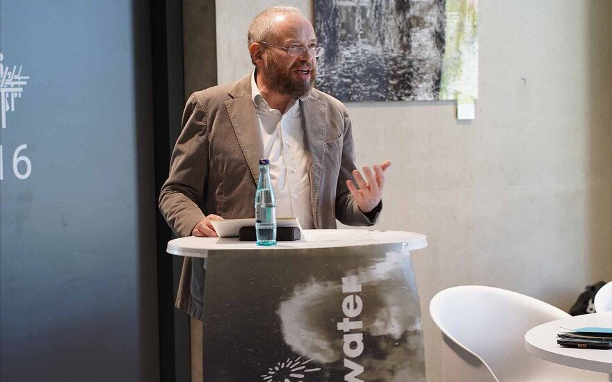 Professor Gawel steht an einem Tisch vor einer Fotografie und hält seine Laudatio