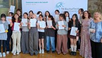 Gruppenfoto mit 20 Personen mit Zertifikaten im Hocksaal vor Logowand