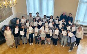 Gruppe der internationalen Kursteilnehmenden, die ihre Zertifikate hochhalten, im Hocksaal der Hochschule