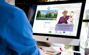 Mann in blauem Hemd sitzt vor einem Monitor, auf dem die Website des Information Management Instituts sowie das Cover der Studie mit Angela Merkel und einem Roboter zu sehen ist