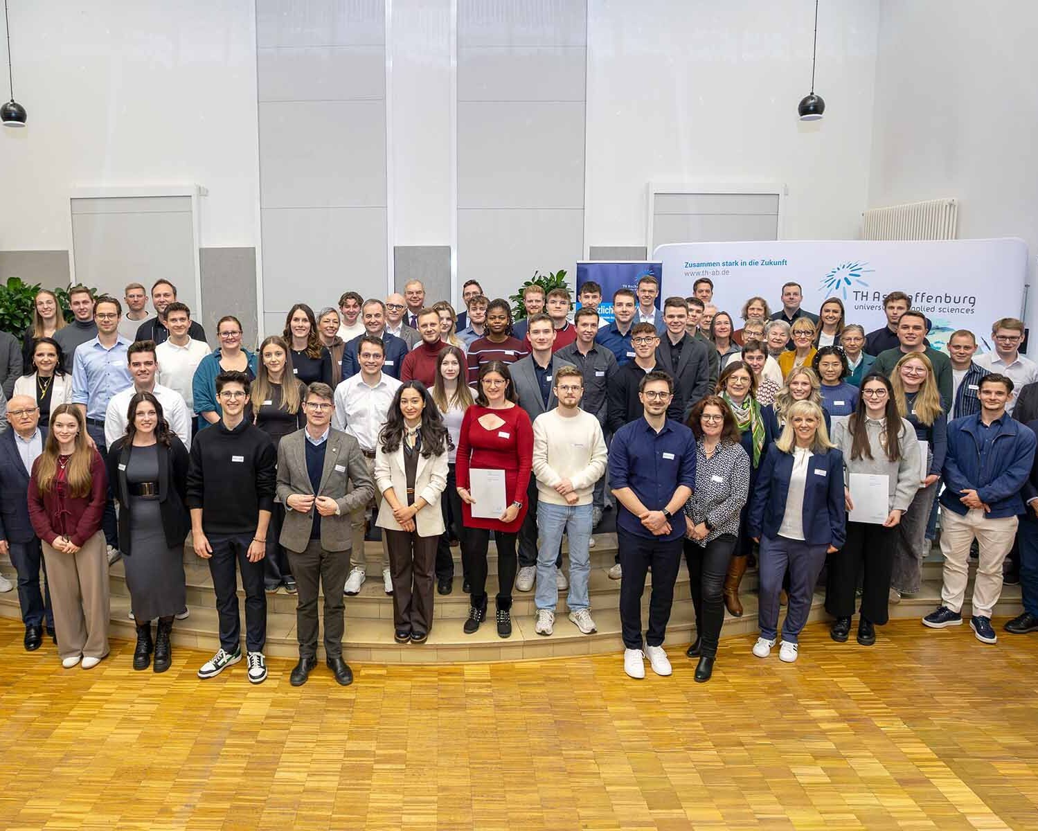 Gruppenbild mit den Fördernden und Stipendiaten in der Aula vor TH-Logowand