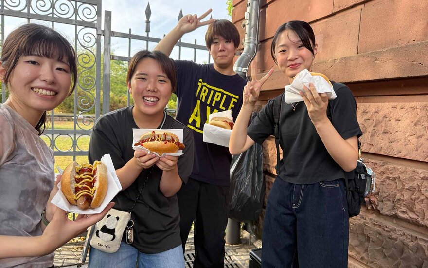 Vier Personen lächeln in die Kamera und halten jeweils eine Bratwurst im Brötchen in der Hand