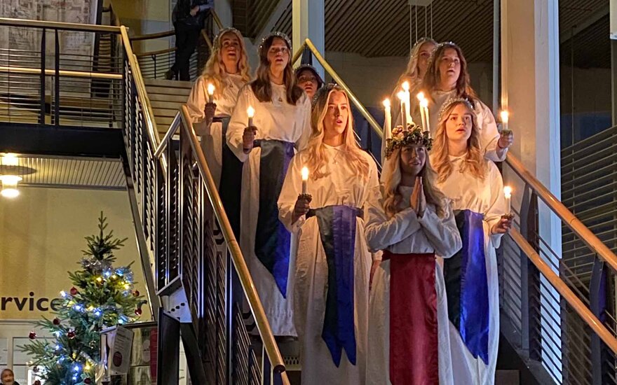 mehrere junge Frauen in weißen Gewändern mit Kerzen in der Hand stehen auf einer Treppe