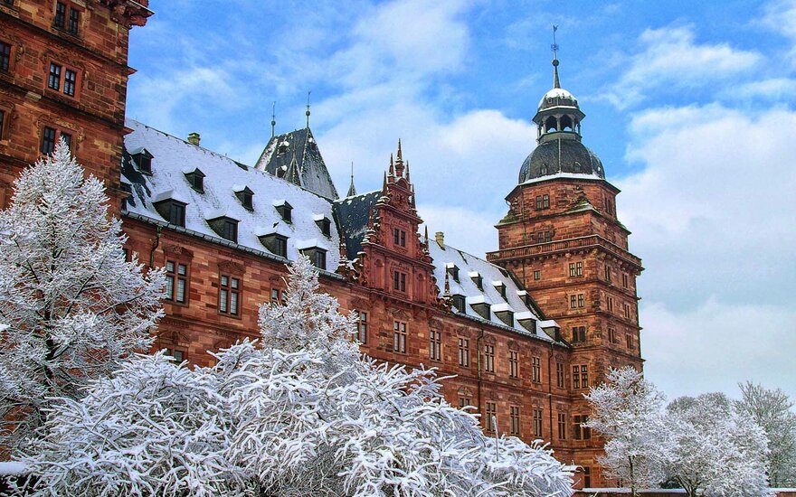 Schräger Blick auf das Aschaffenburger Schloss mit schneebedecktem Dach und Büschen vor leicht bewölktem Himmel