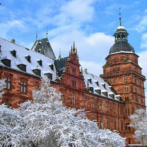 Schräger Blick auf das Aschaffenburger Schloss mit schneebedecktem Dach und Büschen vor leicht bewölktem Himmel