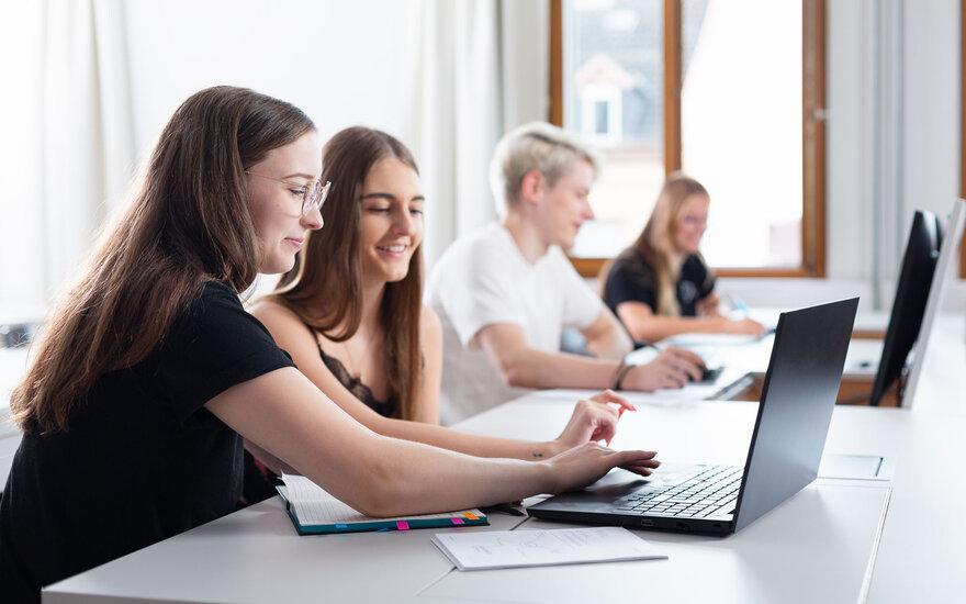 Vier Studierende mit Laptops in Seminarraum von der Seite