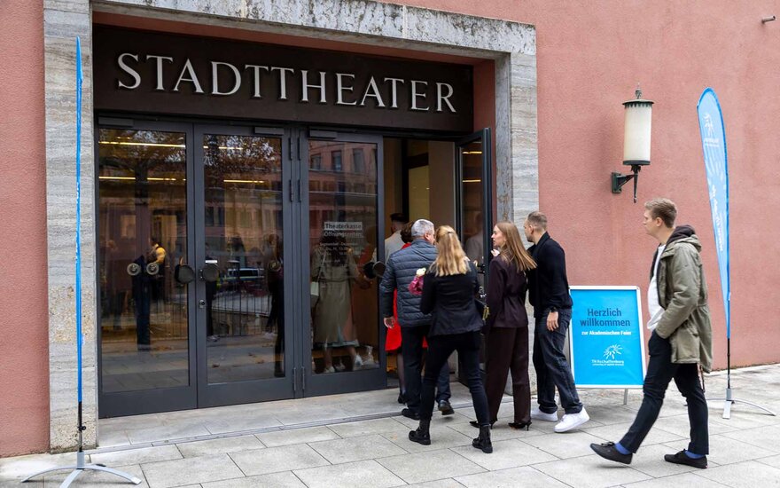 Fünf Personen laufen auf den Eingang des Theaters zu