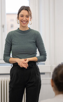Eine junge Professorin steht zwei Personen bei einem Vortrag mit einem Lachen gegenüber. 