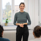 Eine junge Professorin steht zwei Personen bei einem Vortrag mit einem Lachen gegenüber. 