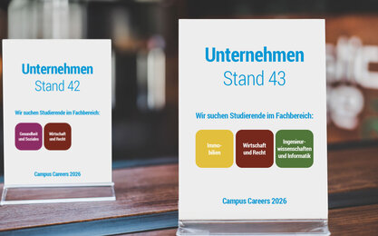 Zwei Tischaufsteller von Unternehmen an einem Messestand kommunizieren die Fachbereiche, in denen sie Studierende suchen.