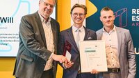 Gewinner mit Urkunde und drei weiteren Männern auf der Bühne
