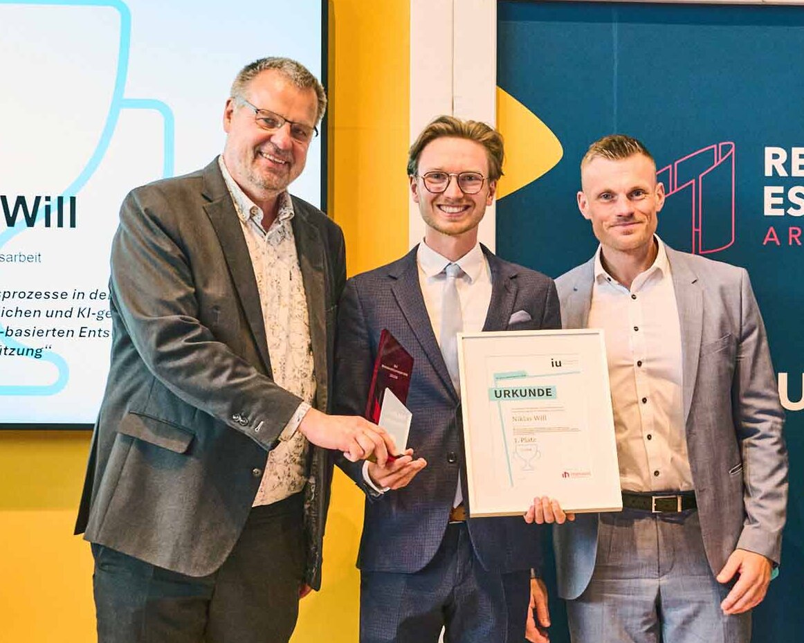 Gewinner mit Urkunde und drei weiteren Männern auf der Bühne