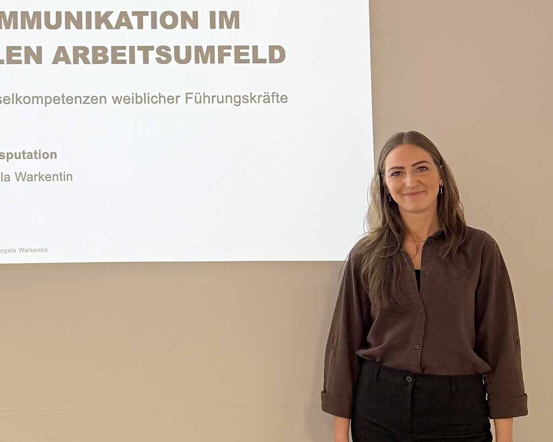 Frau mit langen dunkelblonden Haaren steht vor Leinwand mit Titel ihrer Promotion