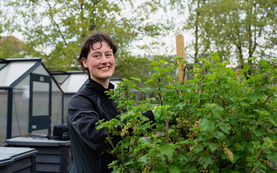 Junge Frau, die im Hochschulgarten arbeitet und in die Kamera lacht