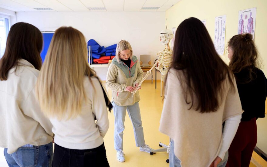 Lehrkraft erklärt vier Auszubildenden Lehrinhalte der Ergotherapie.