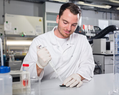 Ein Labormitarbeiter gibt mithilfe einer Laborpipette Flüssigkeit auf einen Sensor.