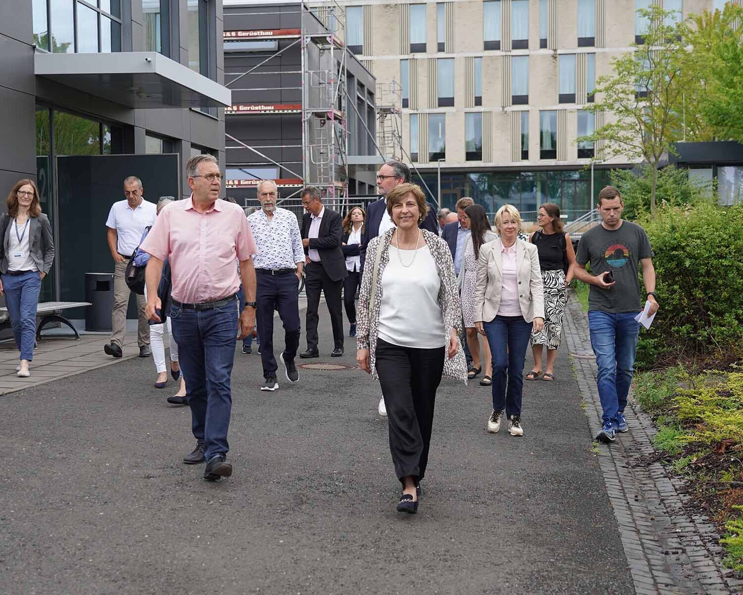 Präsidentin und Oberbürgermeister laufen mit Stadratsmitgliedern auf Weg vor Neubauten