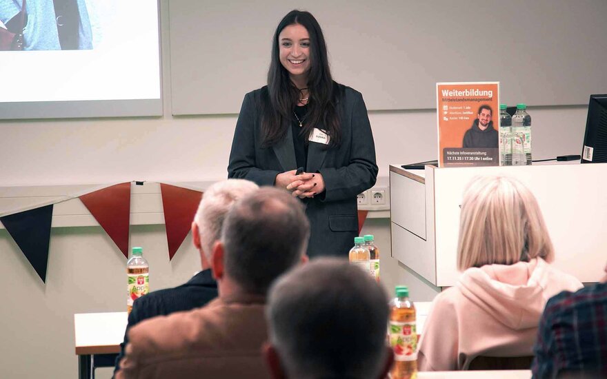 Frau mit langen dunklen Haaren steht im Hörsaal und spricht zu den Teilnehmenden