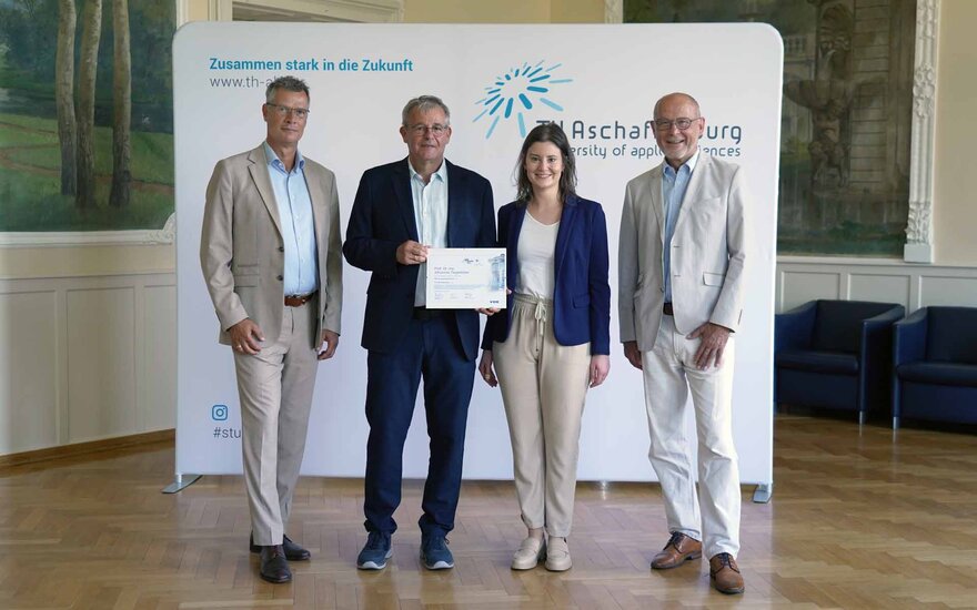 Vizepräsident, neuer VDE-Vertrauensdozent mit Urkunde, Leiterin des VDE Young Net und VDE-Geschäftsführer stehen vor TH-Logo-Wand im Hocksaal