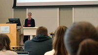 Professorin Balleis am Rednerpult vor Leinwand mit Studierenden im Vordergrund
