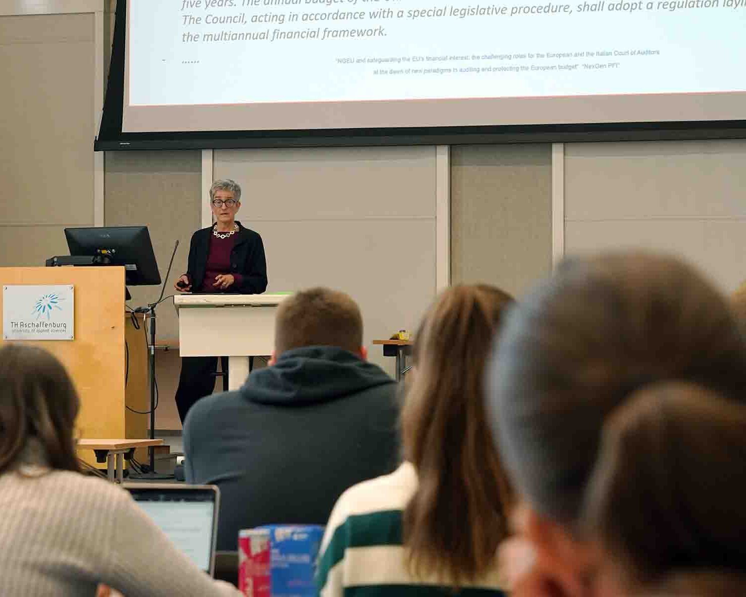 Professorin Balleis am Rednerpult vor Leinwand mit Studierenden im Vordergrund