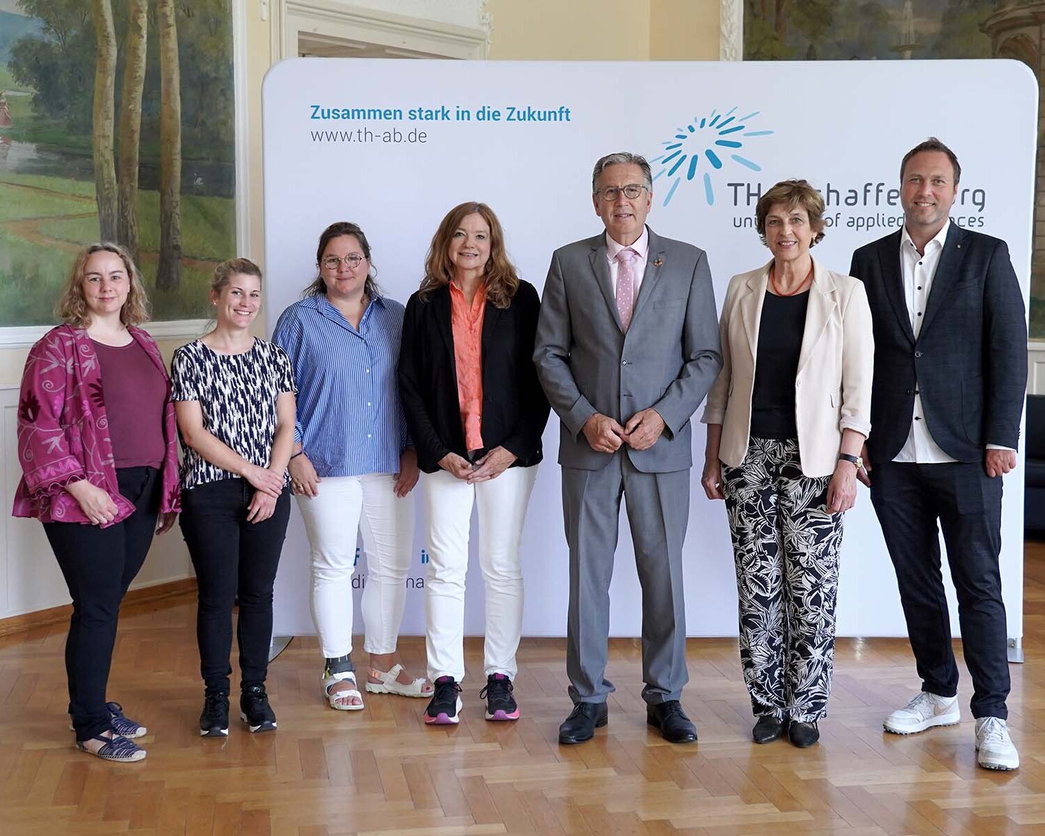 Fünf Frauen und zwei Männer stehen nebeneinander vor weißer Messewand mit blauem TH-Logo im Hocksaal
