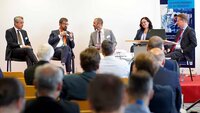 Fünf Personen sitzen auf einem Podium und diskutieren.