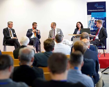 Fünf Personen sitzen auf einem Podium und diskutieren.