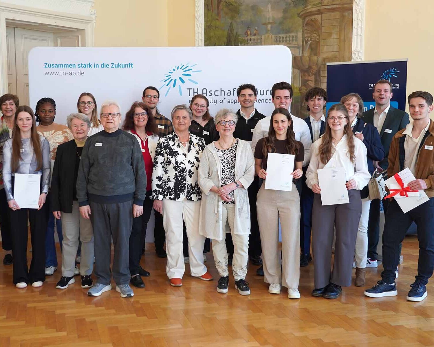 Gruppenfoto von Stipendiaten und Fördernden im Hocksaal vor TH-Logo-Wand