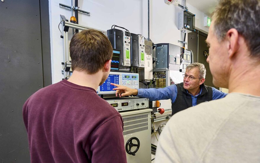 Ein Professor erklärt seinen Mitarbeiterin elektrische Spannungen am Oszilloskop.